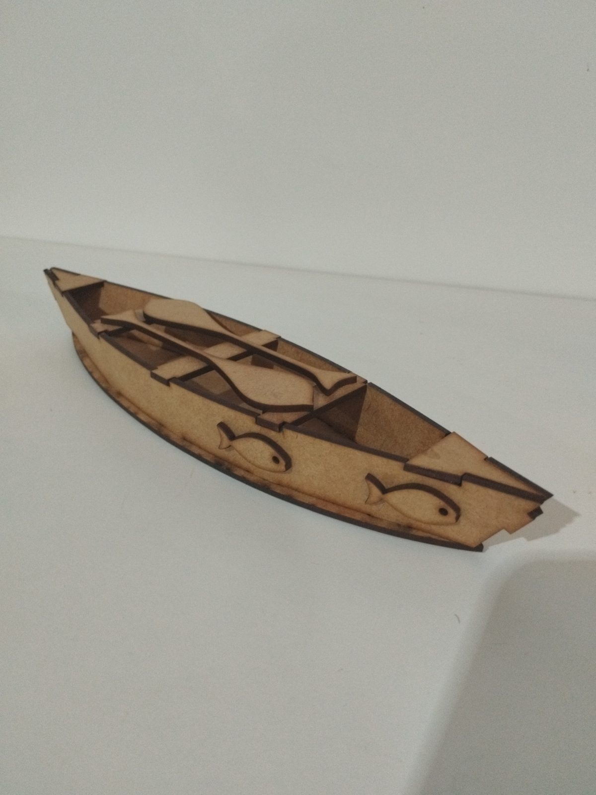 Canoa de madeira em miniatura com desenhos de peixes e remos dentro.