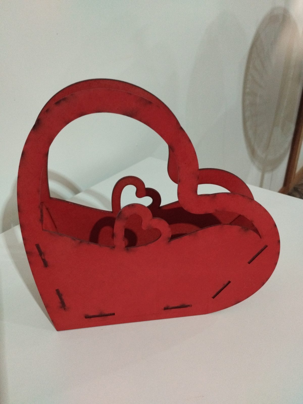 Cestinha de MDF vermelho em formato de coração, com alça e recortes decorativos, sobre superfície branca.