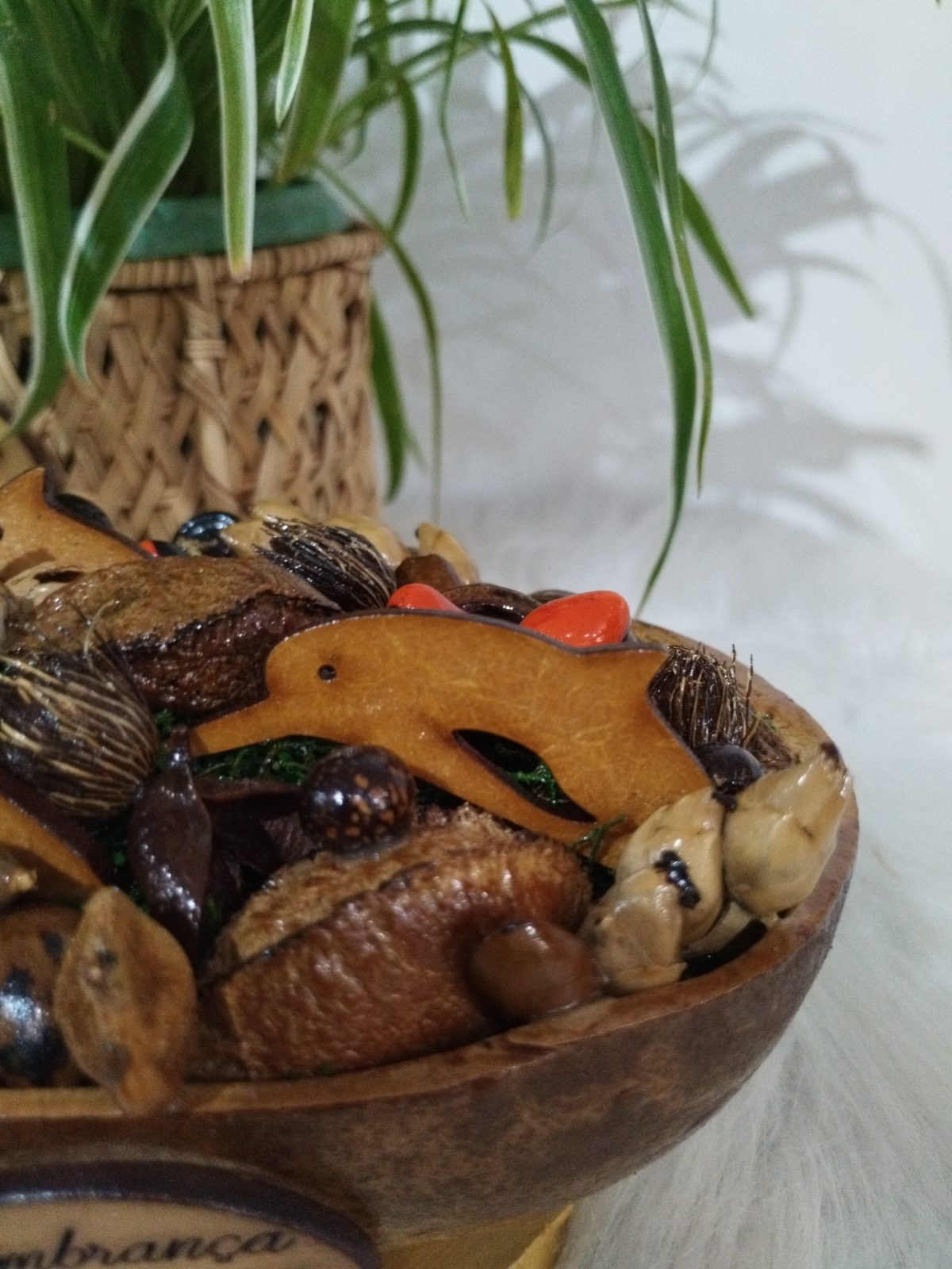 Centro de mesa de cuia em detalhe, com golfinho de madeira entre sementes, fibras e peças vermelhas