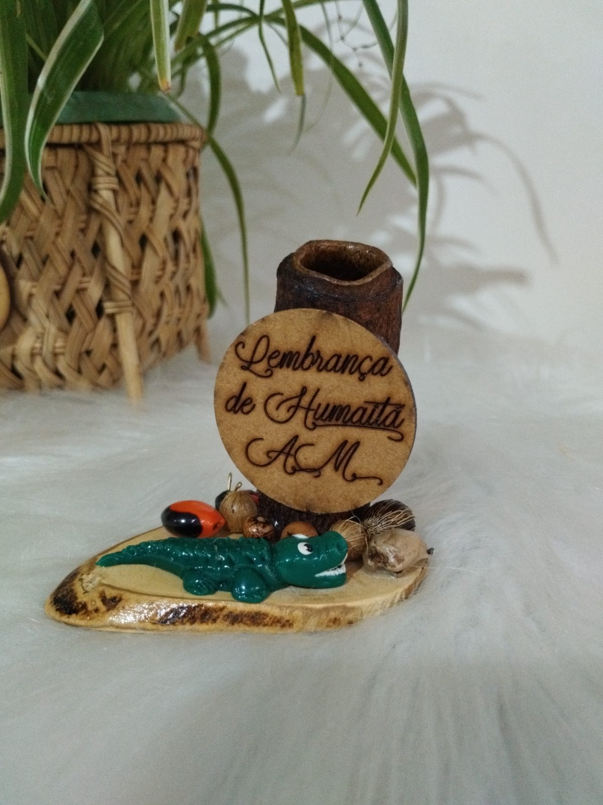 Porta-canetas artesanal com jacaré verde e sementes coloridas na base, com placa escrita Lembrança de Humaitá AM
