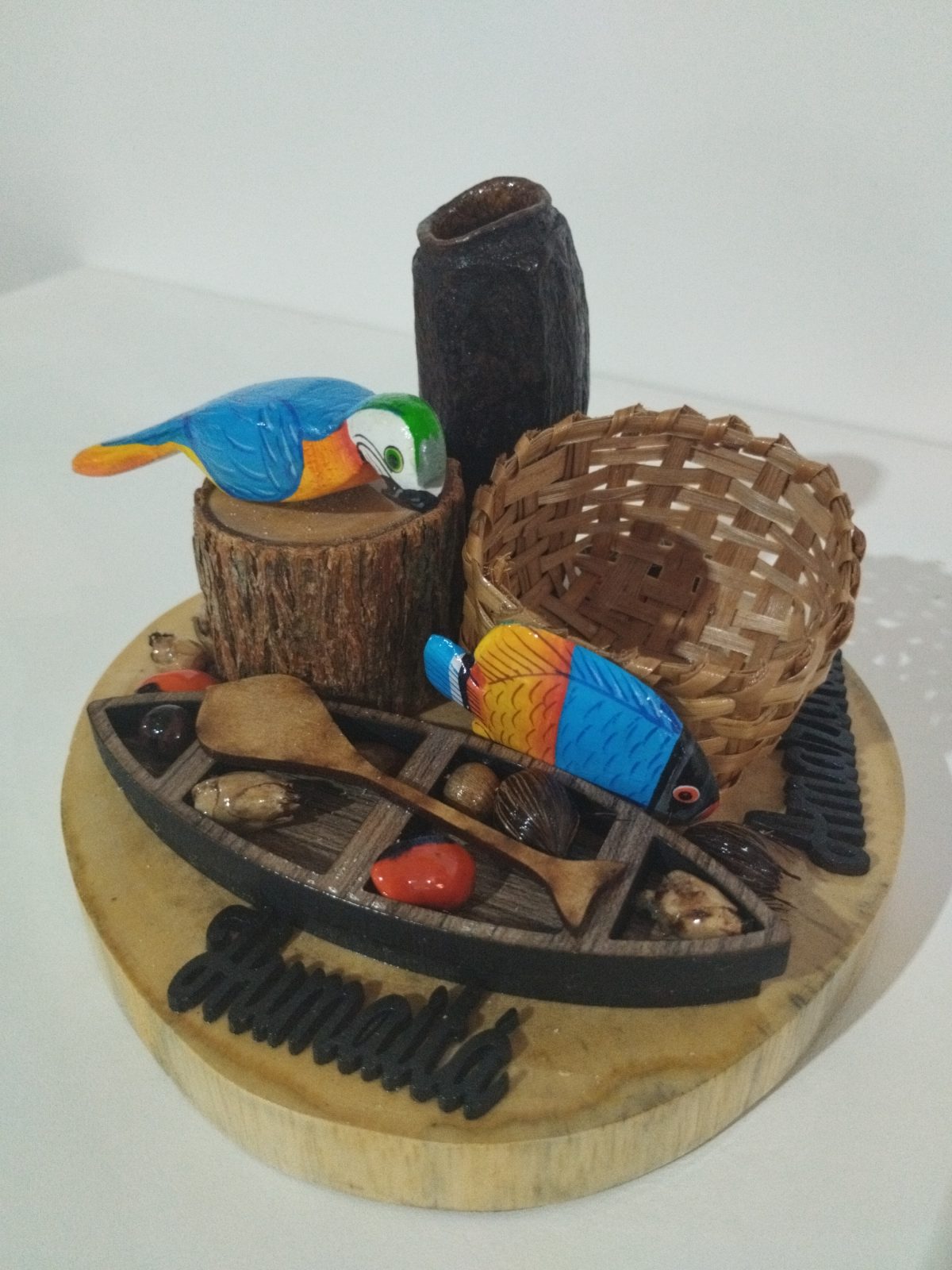 Miniatura regional de Humaitá com canoa em primeiro plano, duas araras, cesto e sementes