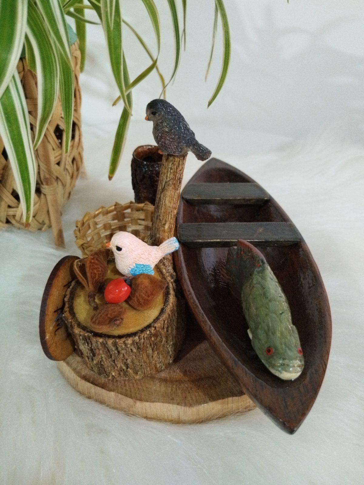 Miniatura de canoa com peixe e dois pássaros, vista lateral com troncos e cesto trançado