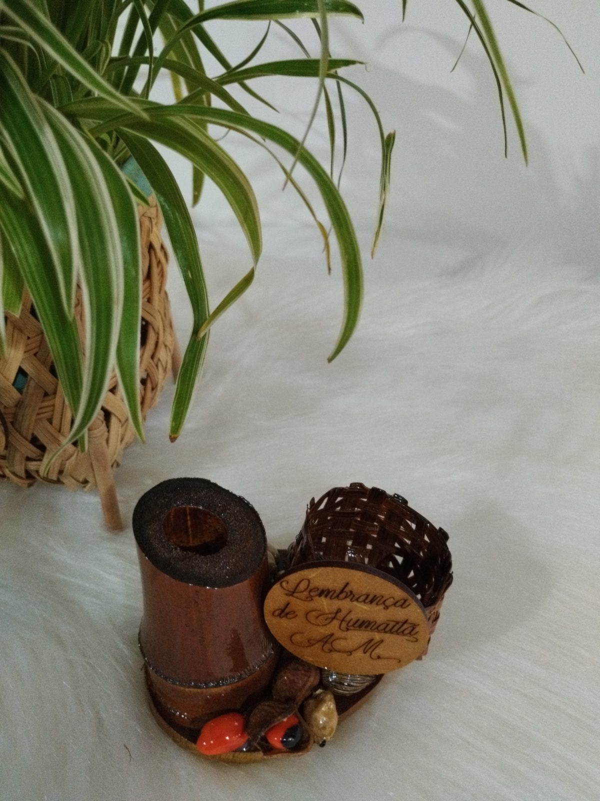 Peça decorativa rústica de bambu e sementes vista inteira ao lado de vaso com clorofito