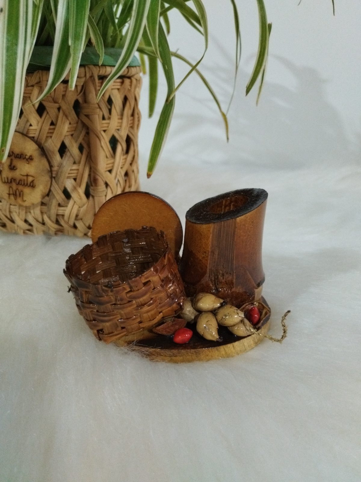 Detalhe de miniatura de cesto de fibra trançada e pedaço de bambu com sementes sobre base de madeira