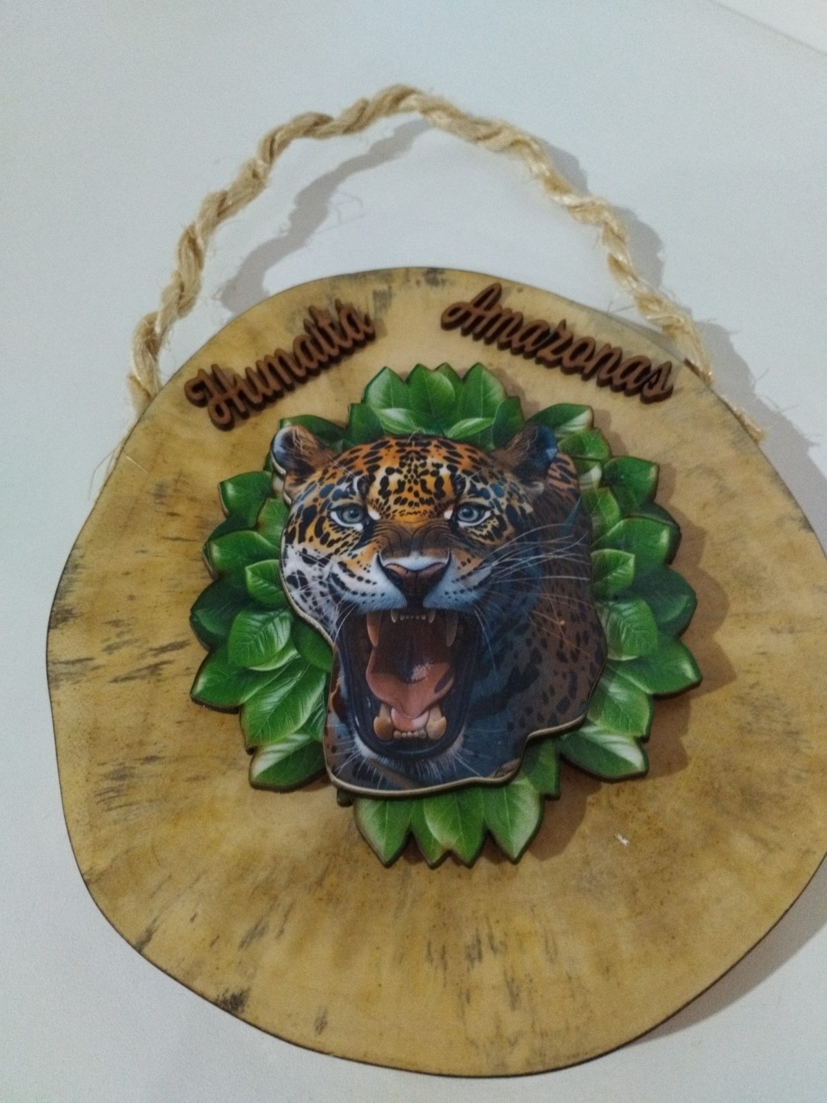 Placa decorativa de Humaitá e Amazonas com onça-pintada de boca aberta entre folhas