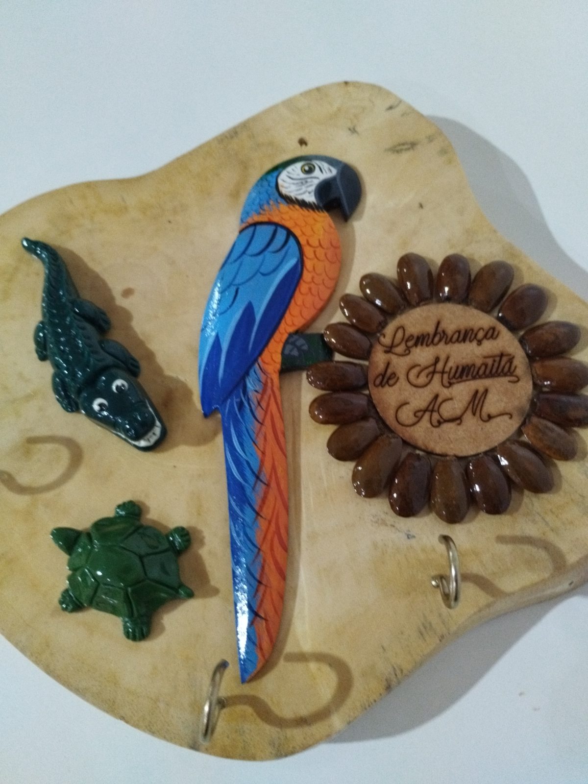 Porta-chaves de madeira em detalhe, com arara-canindé e medalhão de Humaitá cercado por sementes