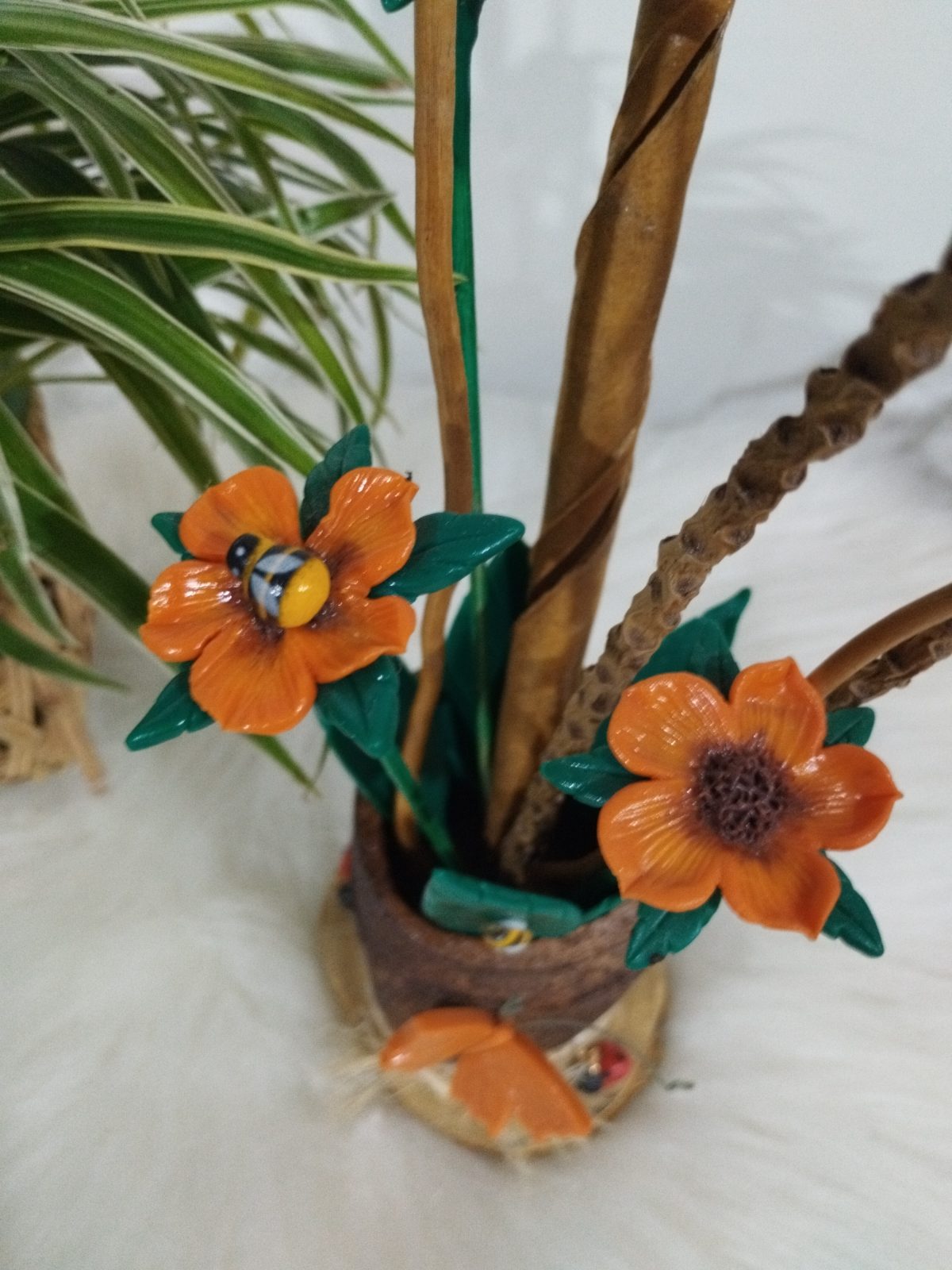 Vaso rústico em detalhe com flores laranjas, folhas verdes e abelha colorida