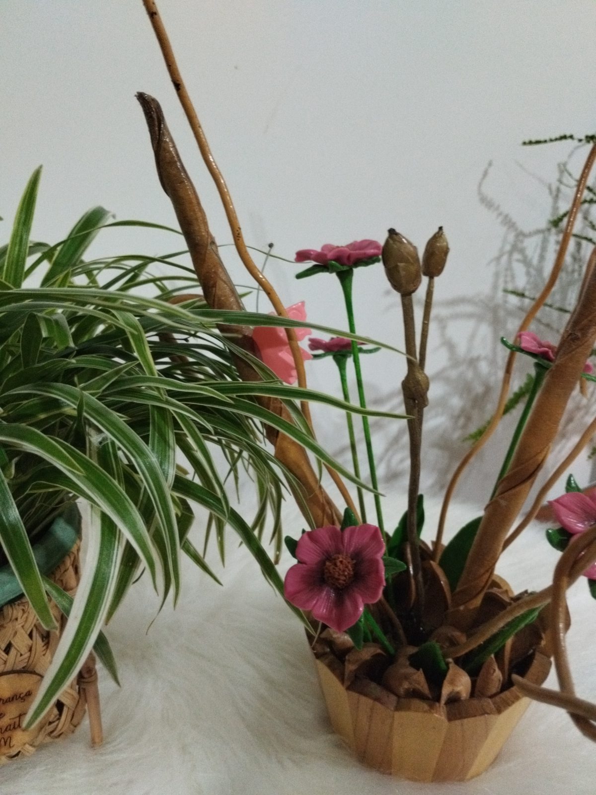 Vaso de madeira visto de lado com flores rosas, botões marrons, folhas verdes e fibras altas