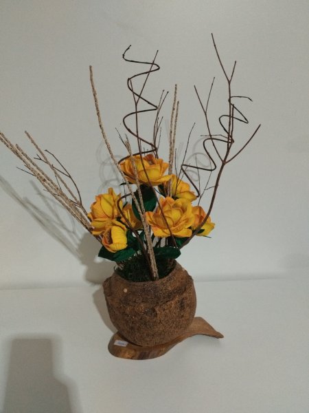 Arranjo de flores amarelas de EVA dentro de uma castanha sapucaia com galhos secos e base de madeira