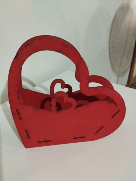 Cestinha de MDF vermelho em formato de coração, com alça e recortes decorativos, sobre superfície branca.
