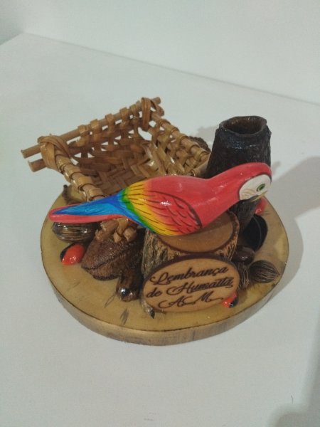 Enfeite de mesa com arara vermelha, cestinha e sementes sobre base de madeira.