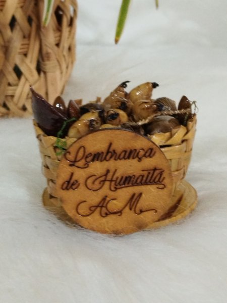 Cestinha trançada de cipó ambé cheia de sementes e com plaquinha de lembrança.
