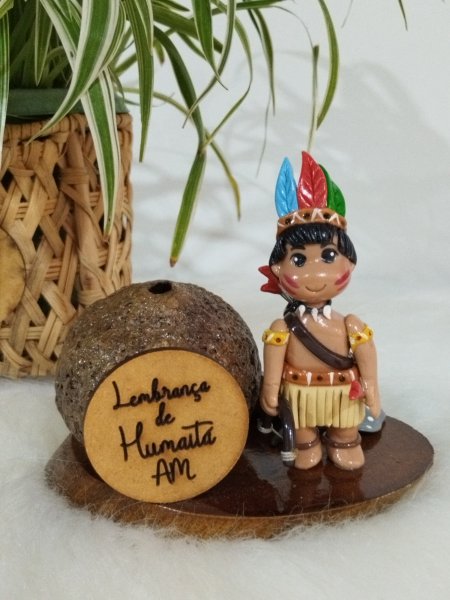 Miniatura de índio com cocar colorido e arco ao lado de tronco em base de madeira.