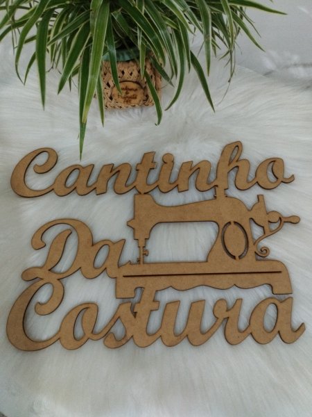 Placa em MDF cru com a frase Cantinho da Costura e desenho de máquina de costura.