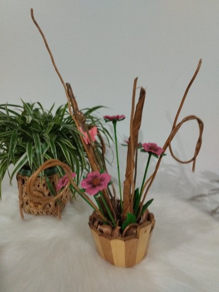 Vaso de madeira listrado com galhos secos e flores cor-de-rosa artificiais em cima de uma base branca.