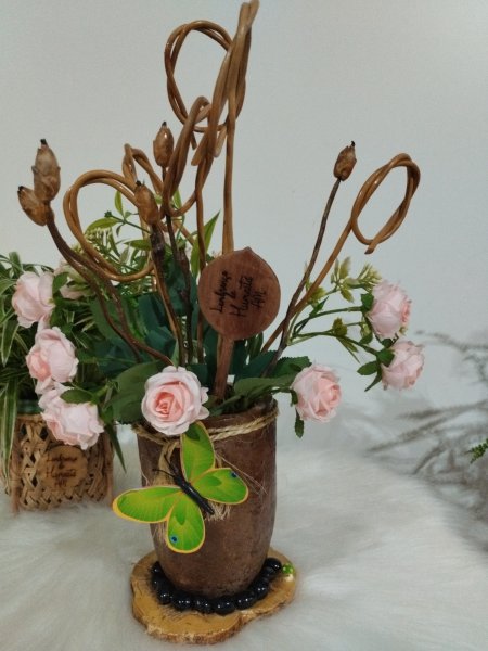 Vaso marrom com rosas cor-de-rosa, galhos secos e uma borboleta verde aplicada na frente.
